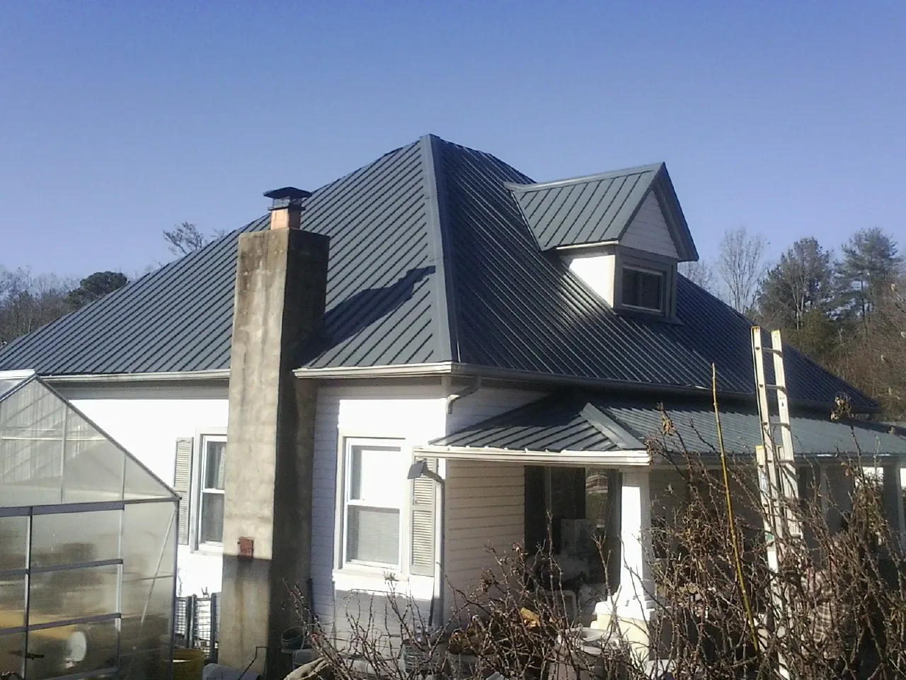 Dark blue standing seam metal roof on a white farmhouse with dormer — Slate & Tile Roof Repair by Roofing Brothers in Upland
