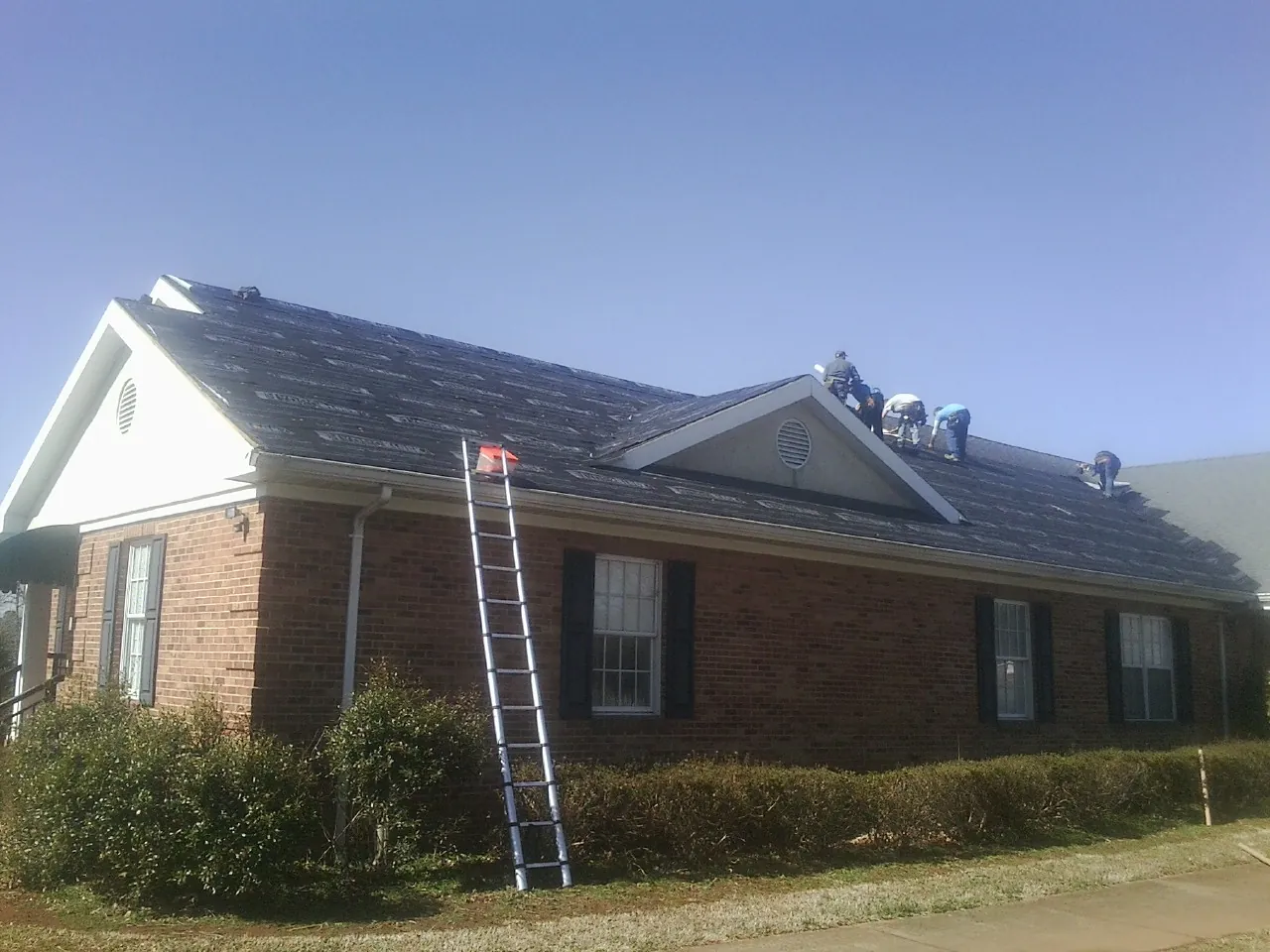 Crew tearing shingles off a brick ranch roof with a ladder set — Metal Roof Repair work by our crew in Upland