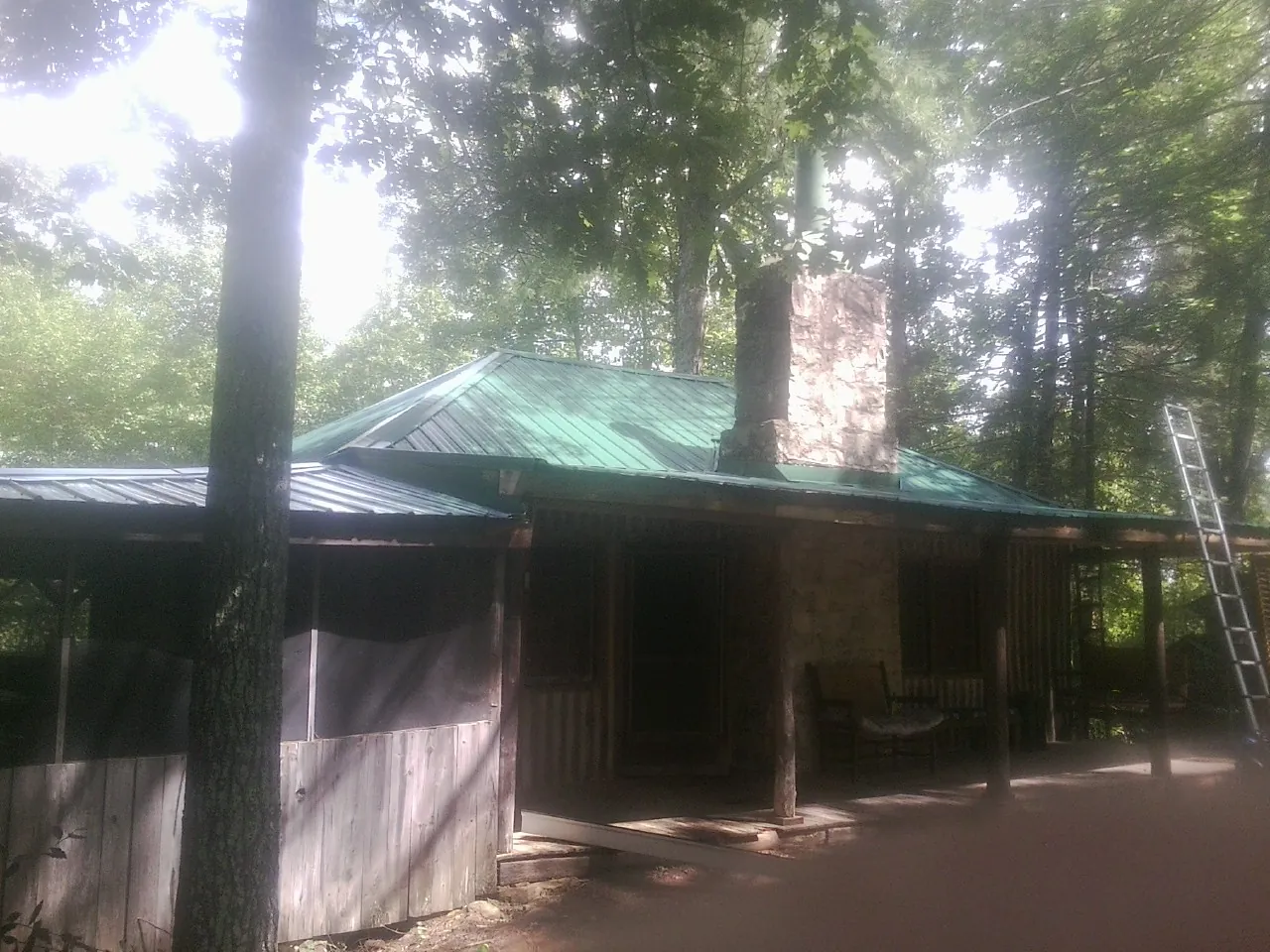 Green metal roof and stone chimney above a log cabin porch in Upland